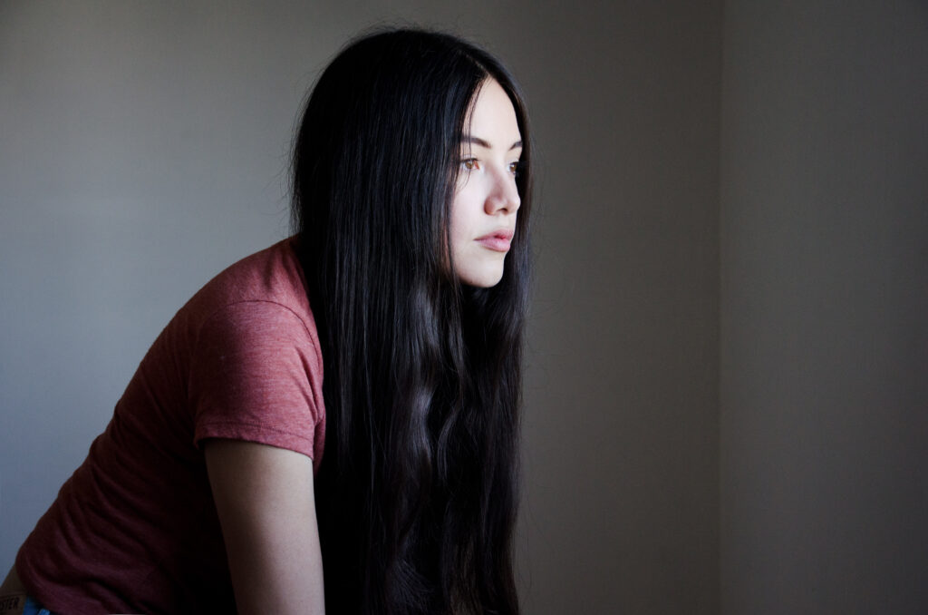Maria Fernanda with long black hair wearing a pink shirt gazes thoughtfully into the distance against a muted background.