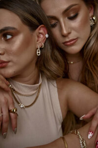Clarisa and Valeria two women with striking features are captured in a close-up shot. They wear intricate jewelry including earrings necklaces and rings. Their makeup is meticulously done with emphasis on their eyes and lips. The image exudes a sense of elegance and sophistication.